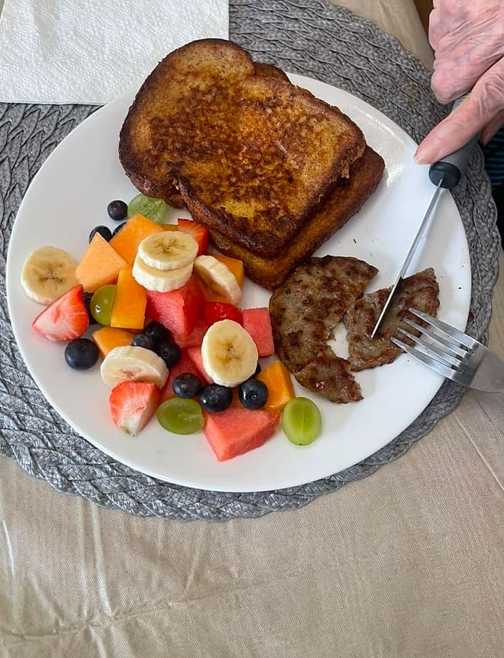A home-cooked breakfast of French toast, fresh fruit and sausage being eaten at Abbey Road Care Homes