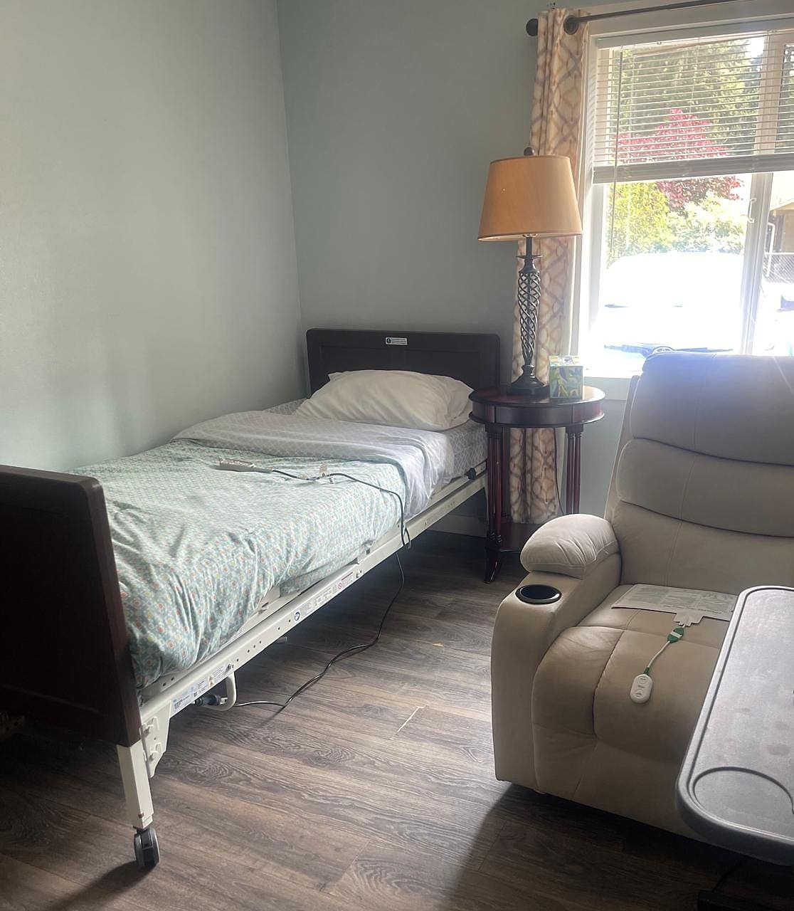 A private bedroom at Abbey Road Care Homes with an adjustable bed, a recliner and a window looking onto the garden