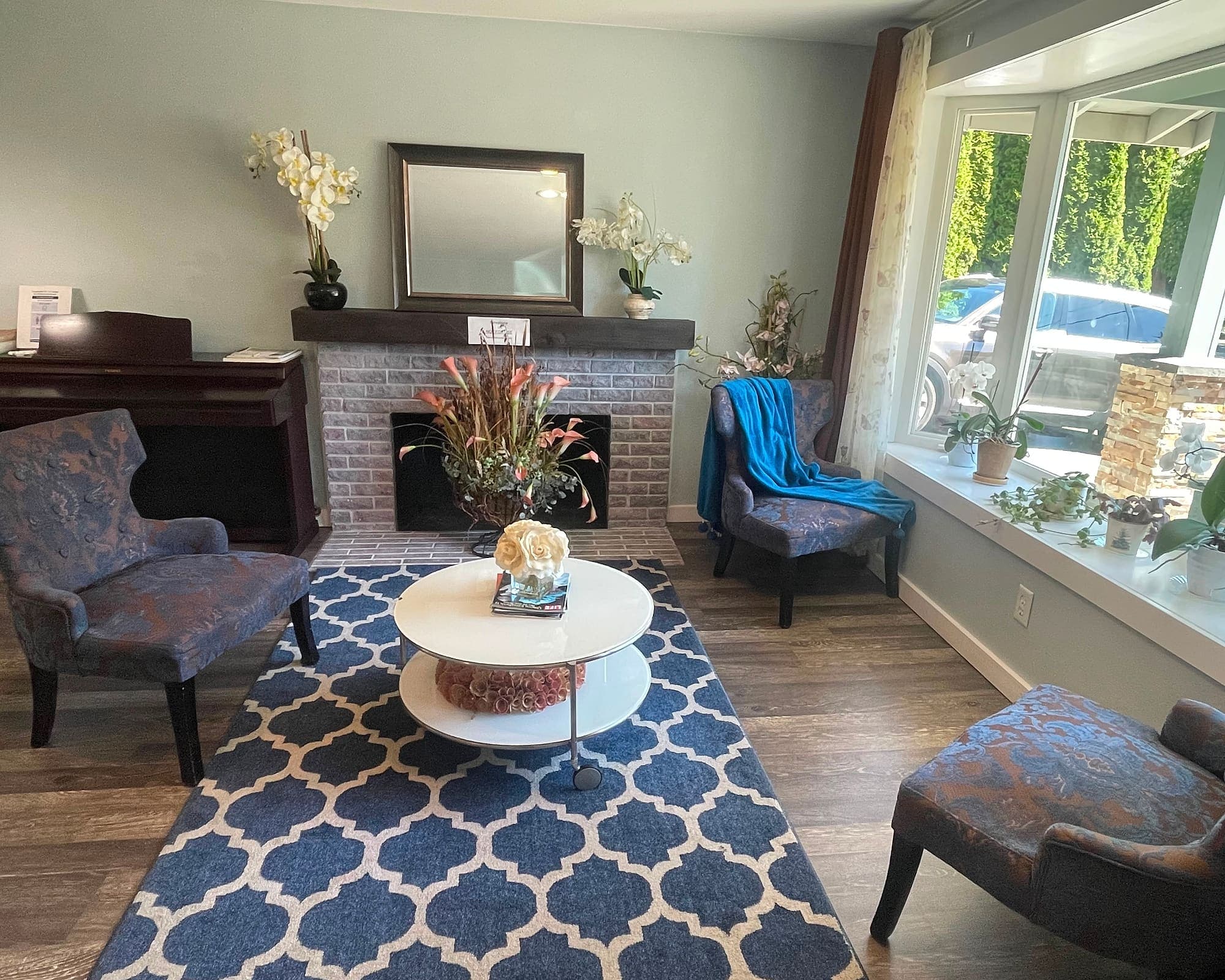 The front sitting room at Abbey Road Care Homes in Edmonds, with patterned armchairs around a fireplace and a bay window of plants
